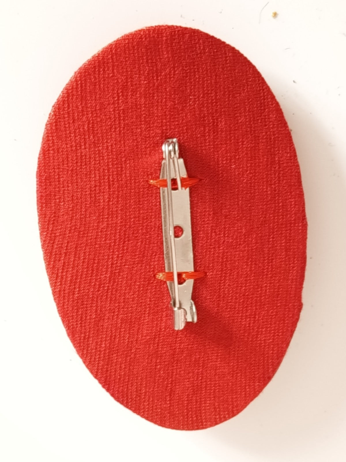Dos de la broche textile rouge montrant un fermoir épingle métallique.