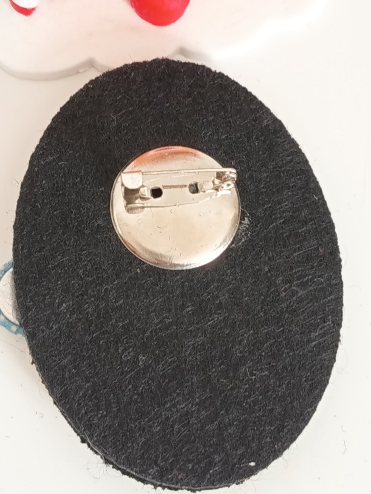 Détail de l'attache métallique argentée au dos de la broche ovale en feutrine noire.