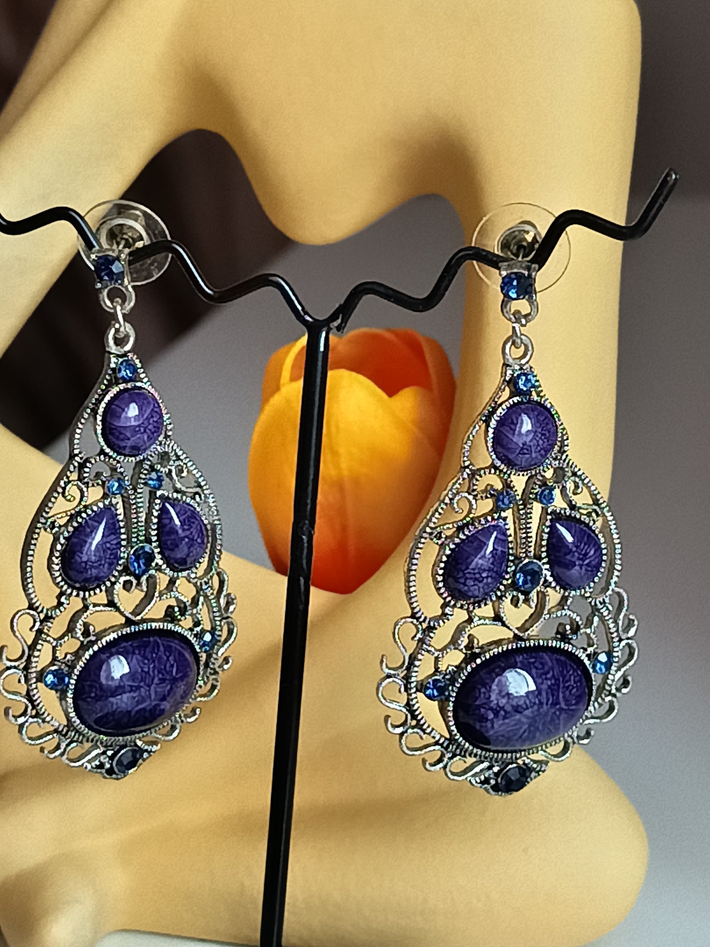 Présentation élégante des boucles d'oreilles pendantes violettes sur un support, mettant en valeur leur design filigrane. 🌸