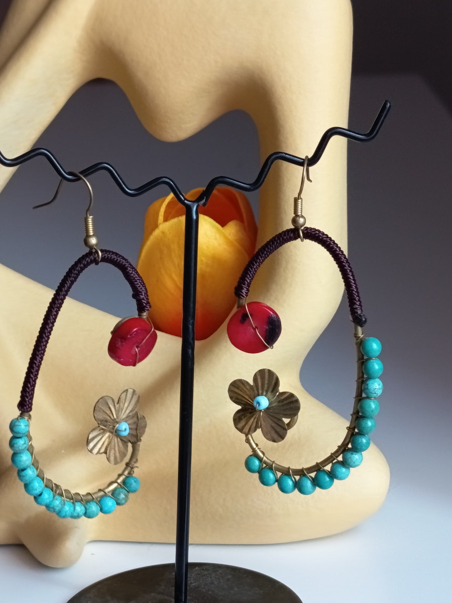 Paire de boucles d'oreilles artisanales créoles ornées de perles turquoise, d'une breloque fleur dorée et d'une perle rouge centrale.