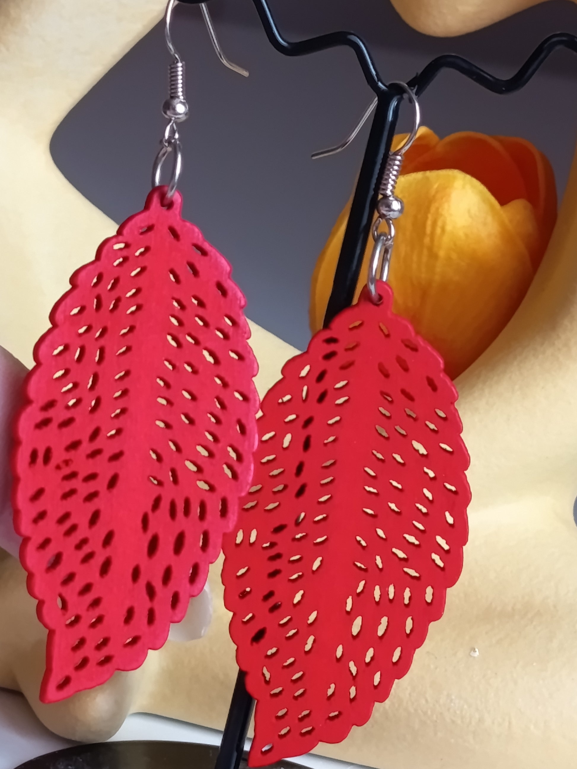 Gros plan sur des boucles d'oreilles rouges en forme de feuille avec motif ajouré sur support noir.