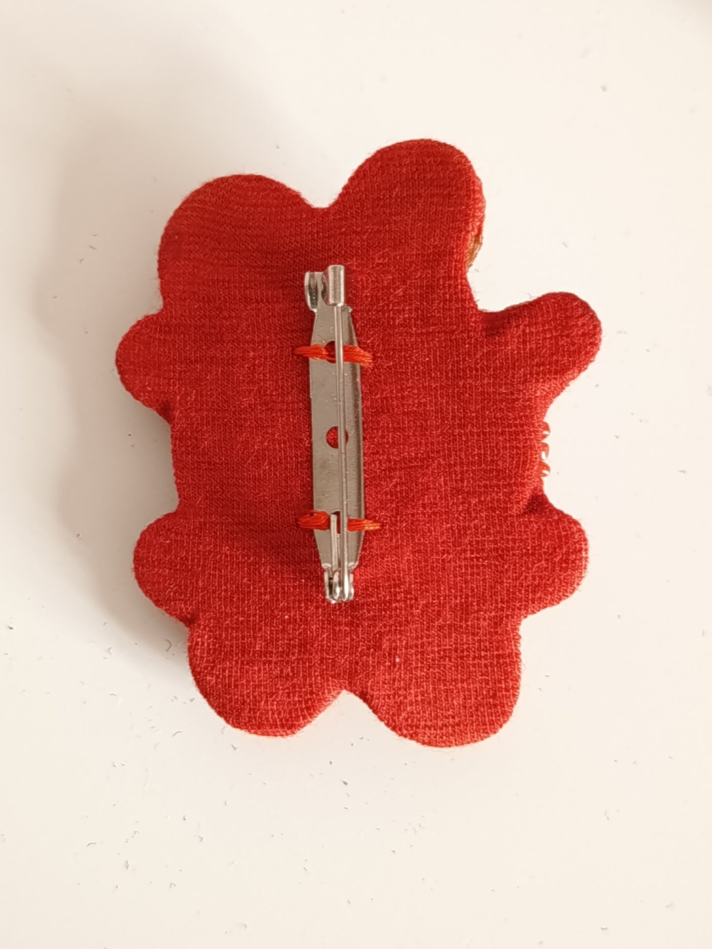 Dos de la Broche avec épingle de sûreté, solidement fixée sur un ond rouge.