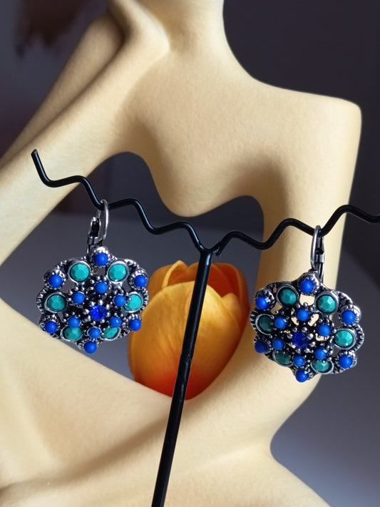 "Paire de boucles d'oreilles pendantes de forme florale avec strass bleus et turquoise sur support de présentation jaune." 👂✨