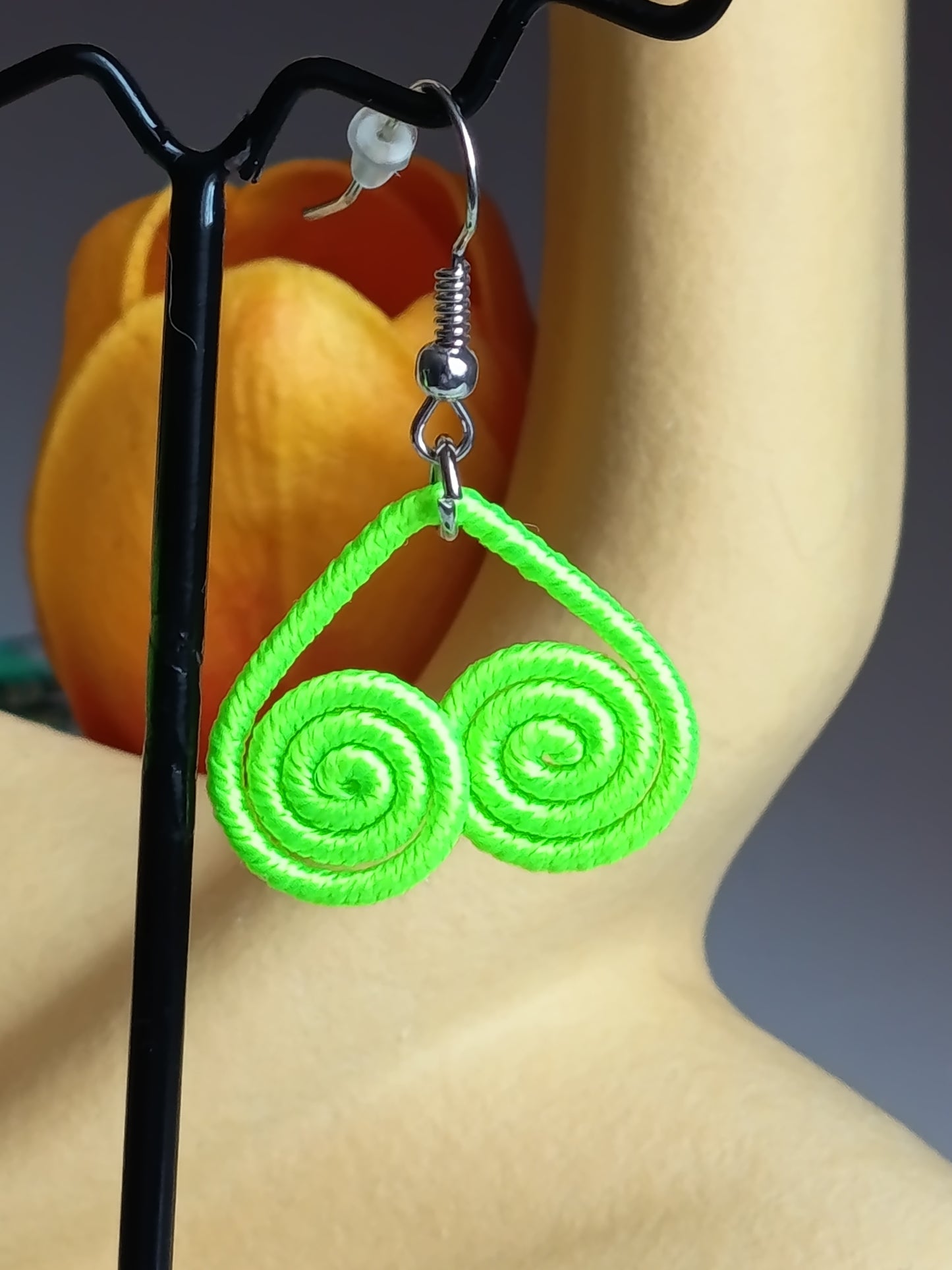 Gros plan sur une seule boucle d'oreille en corde vert néon, montrant la texture tressée et la structure en spirale double, avec le crochet d'oreille couleur argentée  et l'embout en silicone.
